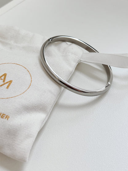 Silver Jayden 4mm smooth oval bangle resting on a branded white linen jewelry pouch.