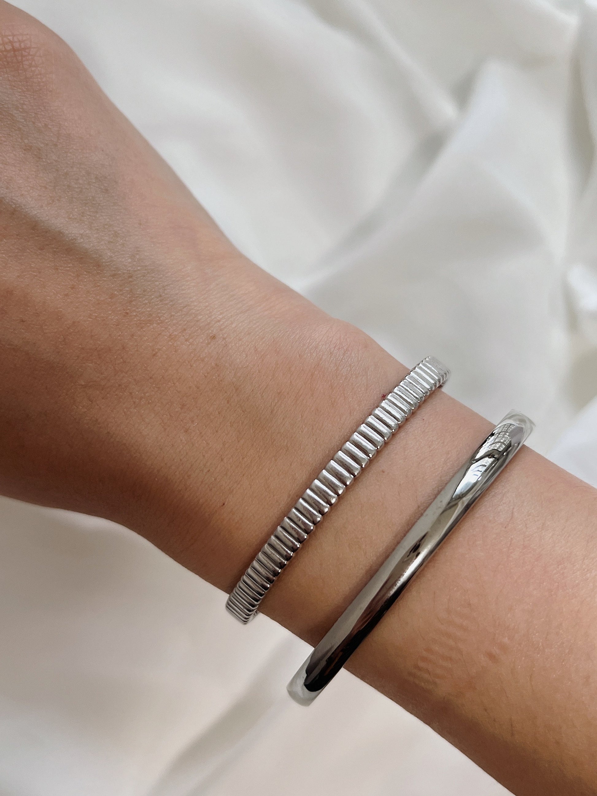Model wrist featuring the silver Jayden 4mm smooth oval bangle paired alongside a ribbed silver bracelet.