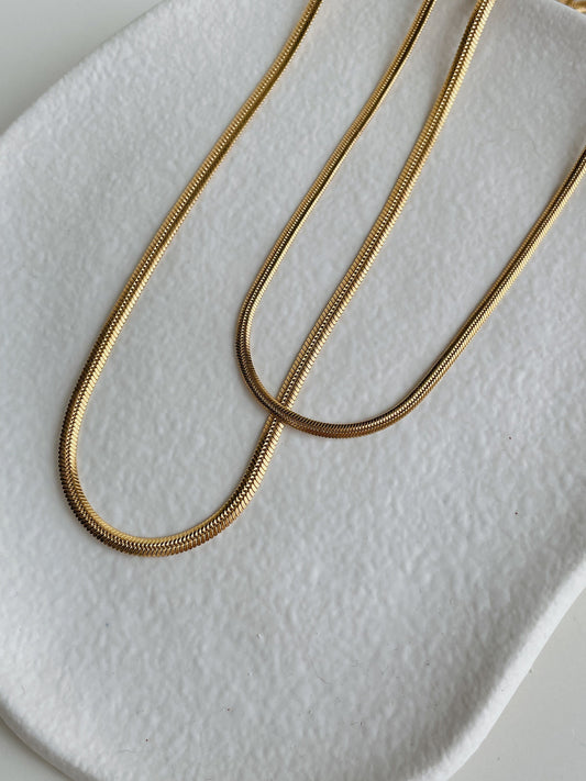 Lola double herringbone chain necklace in 18K gold PVD flat lay on white stone surface, two strands visible