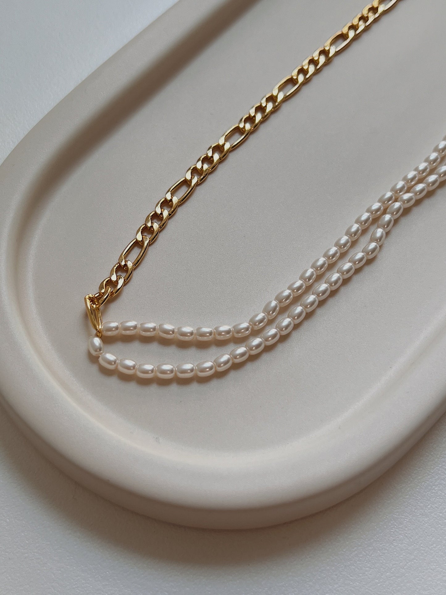 Macro view of heavy 18k gold vacuum plated metal links meeting delicate white pearls