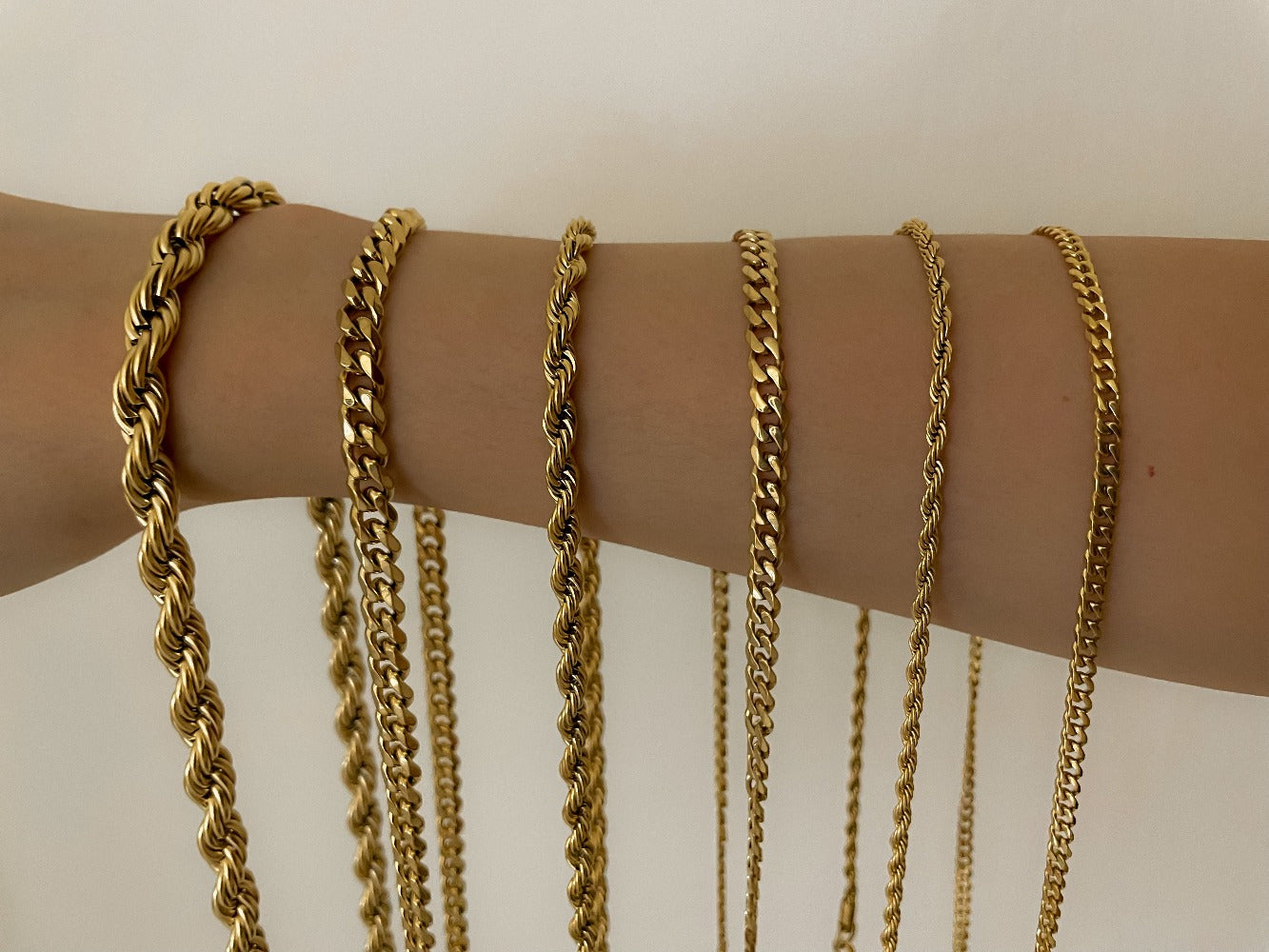 A comparative row of diverse gold chains draped vertically across an arm showcasing variations of a thick helical rope, structured curb link, and fine paperclip necklace