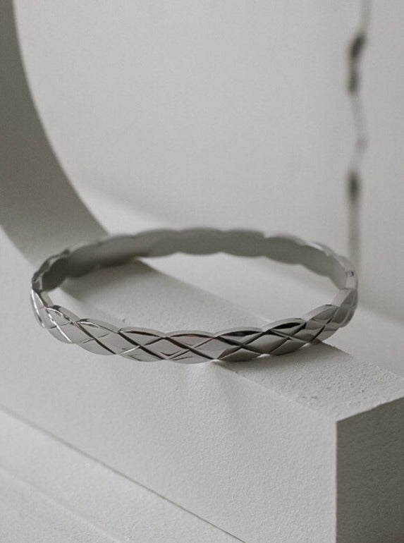 The Corin quilted stacking bracelet in a polished silver rhodium finish, resting horizontally to showcase its sleek, low-profile fit and structural diamond-cut relief.