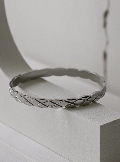 The Corin quilted stacking bracelet in a polished silver rhodium finish, resting horizontally to showcase its sleek, low-profile fit and structural diamond-cut relief.