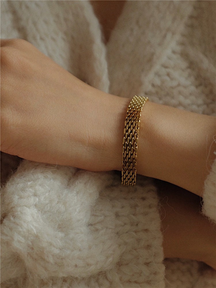 A close-up shot of the Danielle gold mesh chain bracelet worn on a model's wrist against the sleeve of a cozy, off-white chunky knit sweater.