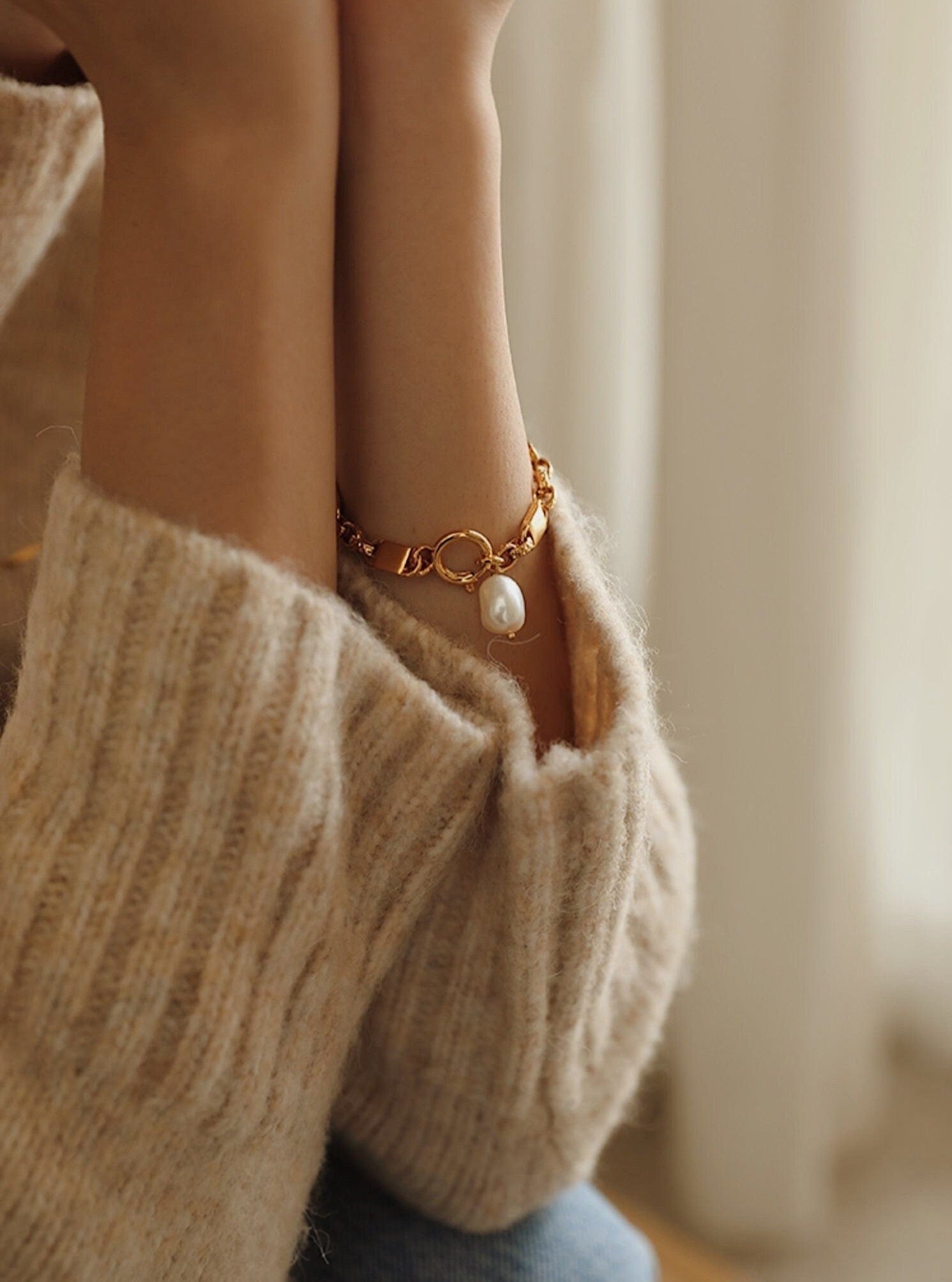 A detailed shot of the Diana gold baroque pearl bracelet on a wrist, resting perfectly against a cozy cream knit sweater cuff.