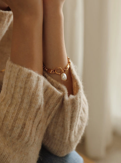 A detailed shot of the Diana gold baroque pearl bracelet on a wrist, resting perfectly against a cozy cream knit sweater cuff.