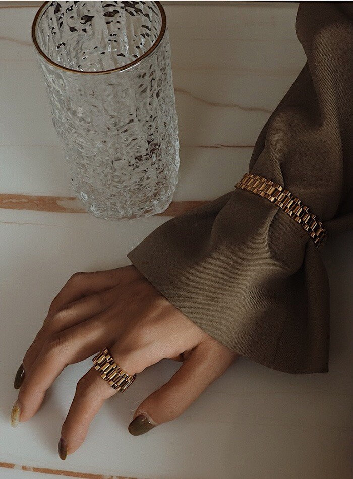 Editorial hand shot of gold watch band ring paired with a timeless watch chain bracelet