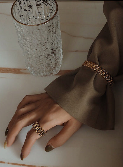 Editorial hand shot of gold watch band ring paired with a timeless watch chain bracelet