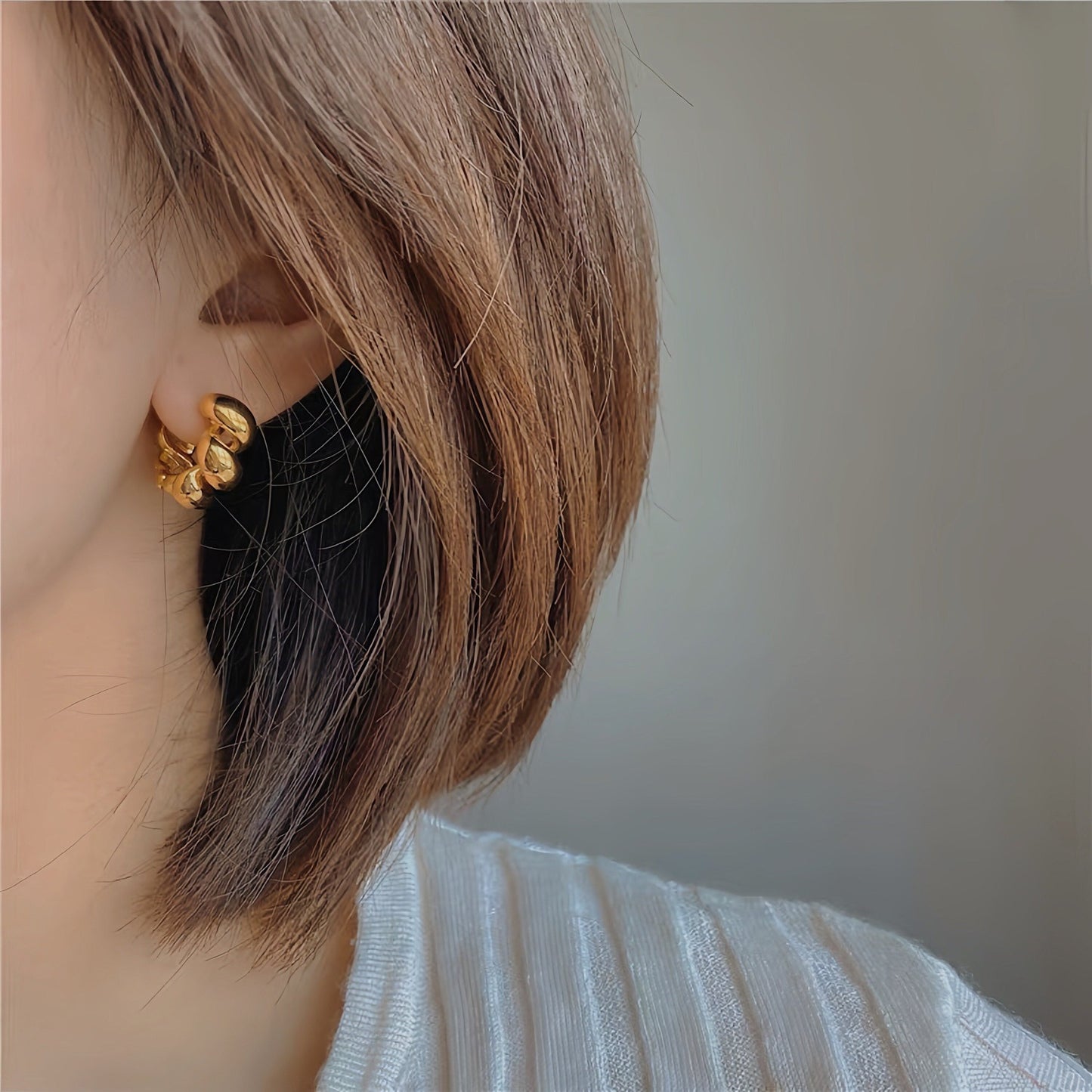 Close up of woman's ear featuring a pair of stunning 18K gold twisted hoop earrings for everyday