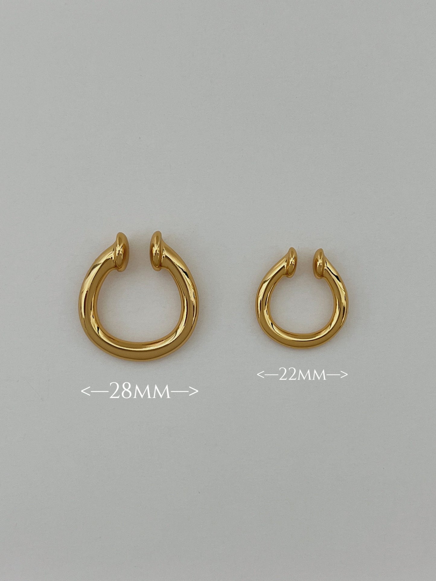 Gold ear cuff earring on white surface, showcasing different sizes of the ear cuff