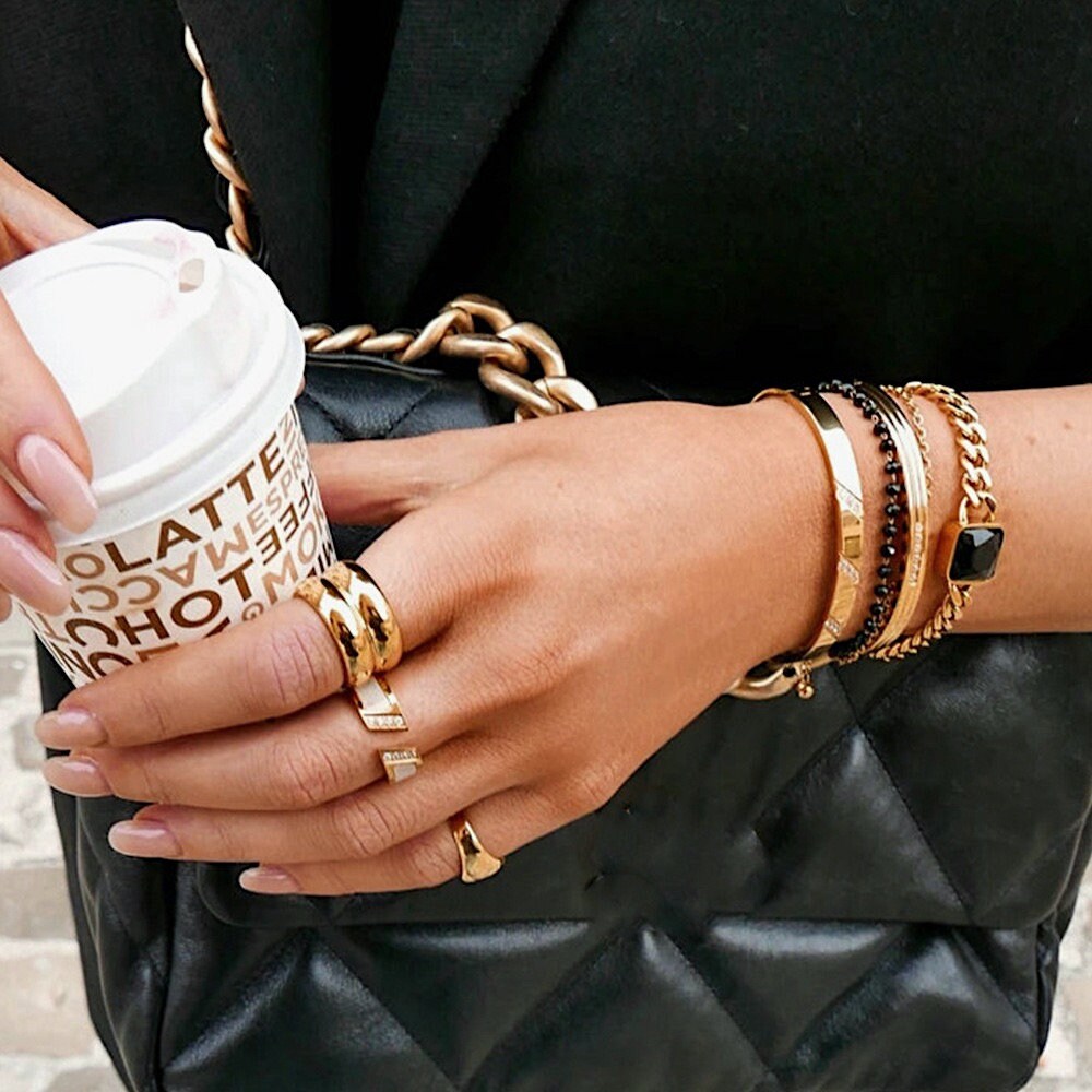 Luxe editorial hand shot of gold chunky band and layering bracelets with neutral nails