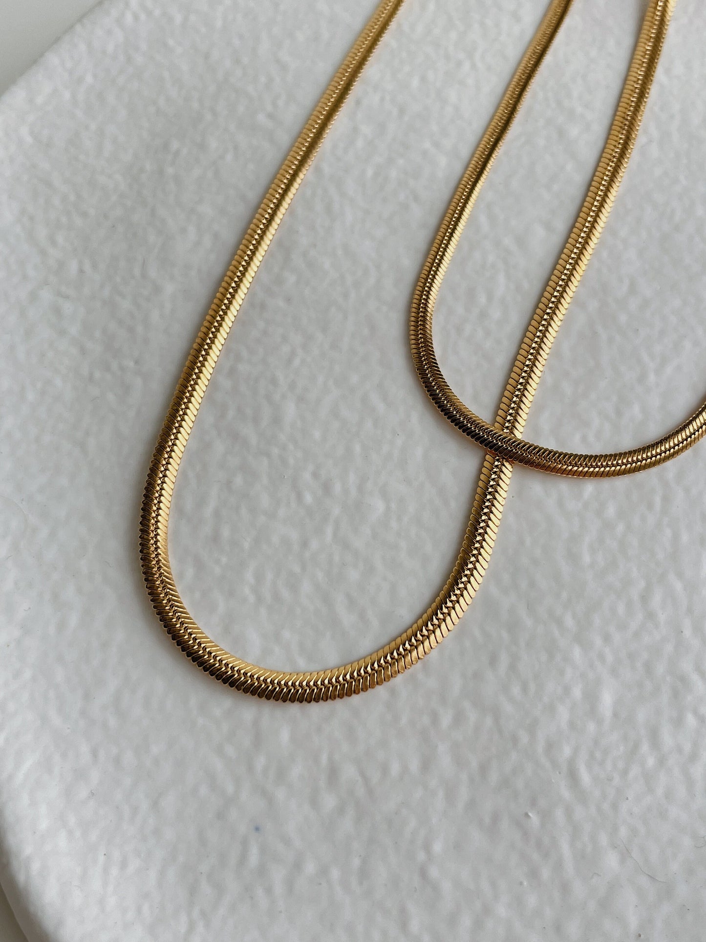 Close-up detail of 18K gold herringbone chain weave texture, warm gold tone, brass base with PVD finish