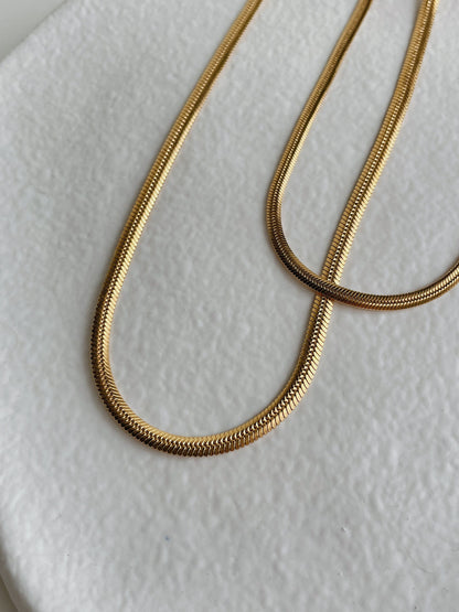 Close-up detail of 18K gold herringbone chain weave texture, warm gold tone, brass base with PVD finish