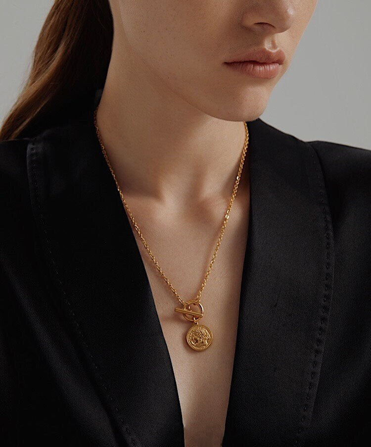 Model wearing a minimalist gold pendant necklace styled with a stack of gold chains.
