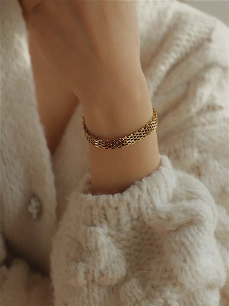 An editorial lifestyle portrait of a model styled in gold jewelry, spotlighting the reflective metal shine of the wide Danielle mesh chain bracelet.