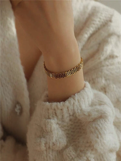 An editorial lifestyle portrait of a model styled in gold jewelry, spotlighting the reflective metal shine of the wide Danielle mesh chain bracelet.