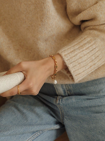 An editorial lifestyle image spotlighting the natural movement of the Diana gold pearl link bracelet as a model holds a magazine.