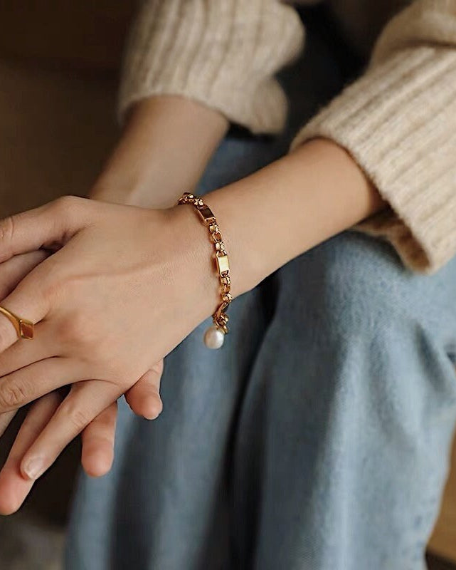 A model wearing the Diana gold pearl chain bracelet on her wrist, paired with a matching gold signet ring and relaxed denim.