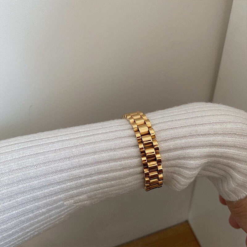 Female model wearing 10mm Spencer watch band bracelet stacked with gold rings and white ribbed knit top.