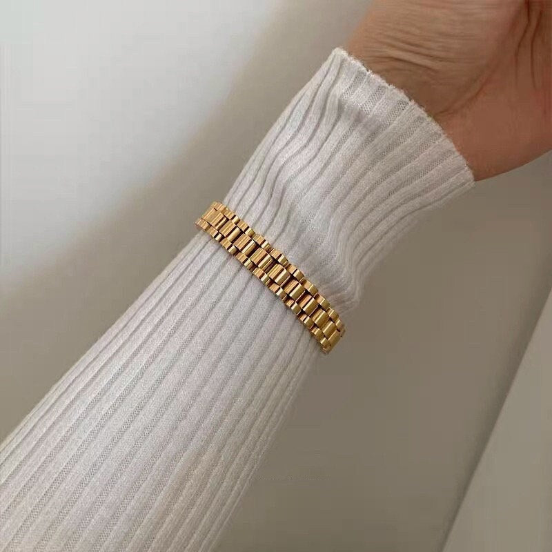 Model wrist detail wearing the 10mm wide gold watch strap bracelet with white ribbed knit top.