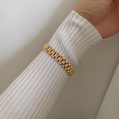 Model wrist detail wearing the 10mm wide gold watch strap bracelet with white ribbed knit top.