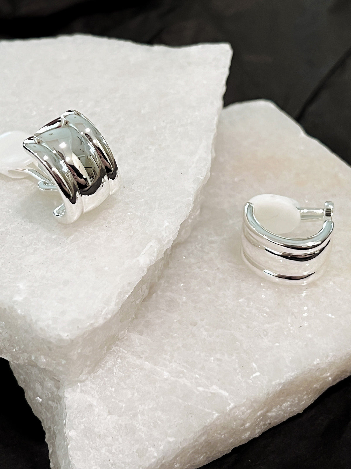 Pair of silver Molly vintage ribbed clip-on earrings on white marble showing high-shine front curve and hinged clip mechanism
