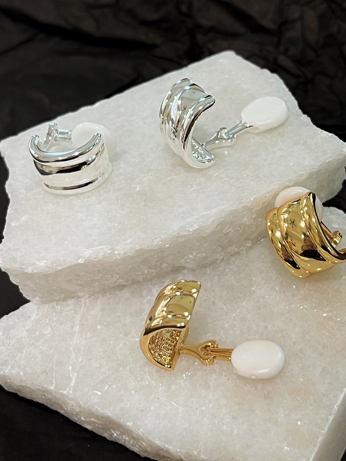 Molly vintage ribbed clip-on earrings displayed on white stone showing gold and silver finishes with white silicone comfort cushion backings