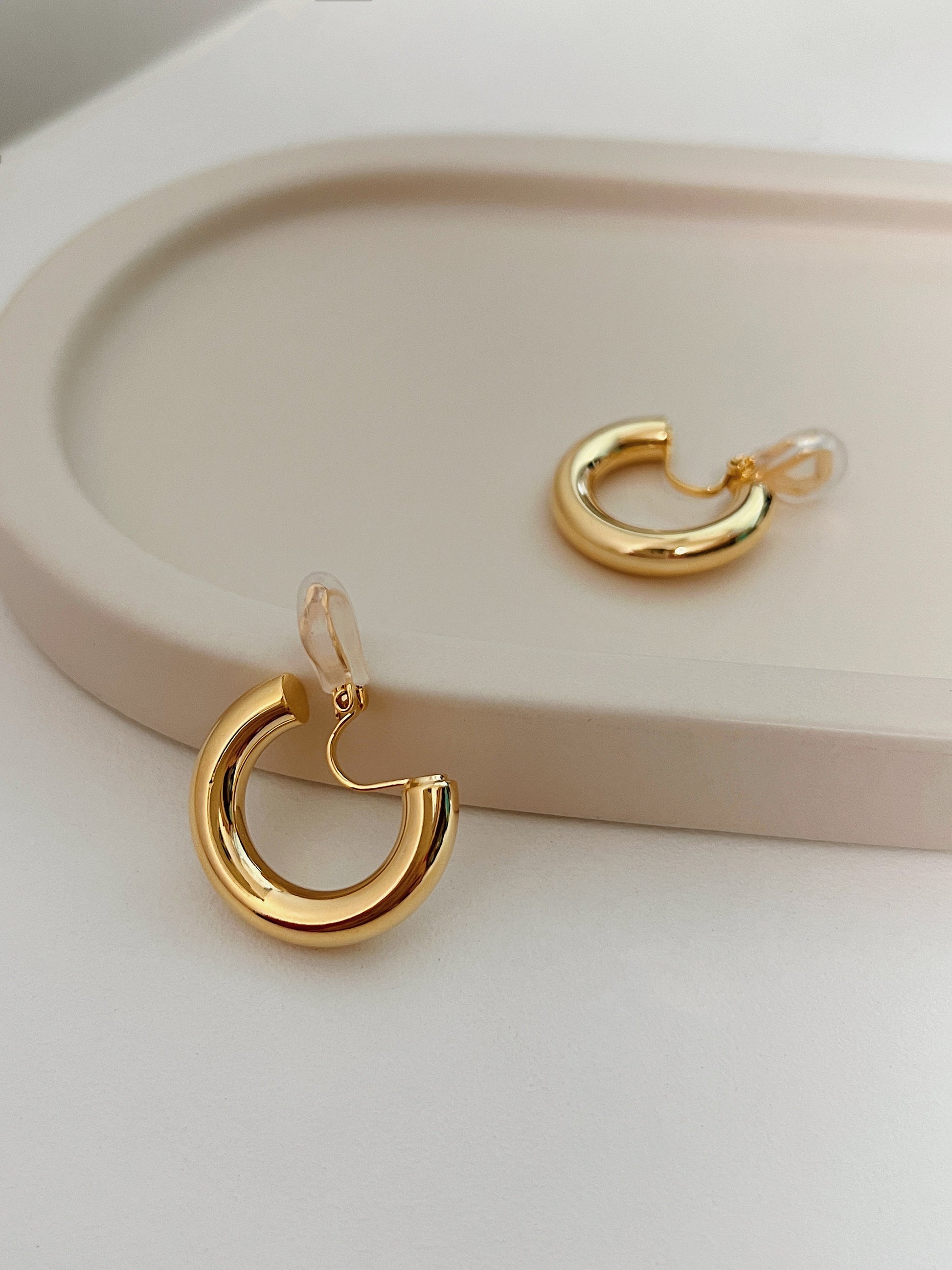 Symmetrical layout of two chunky gold hoop clip earrings revealing the smooth inner curve and adjustable hinge