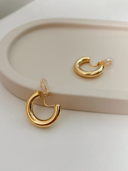 Symmetrical layout of two chunky gold hoop clip earrings revealing the smooth inner curve and adjustable hinge