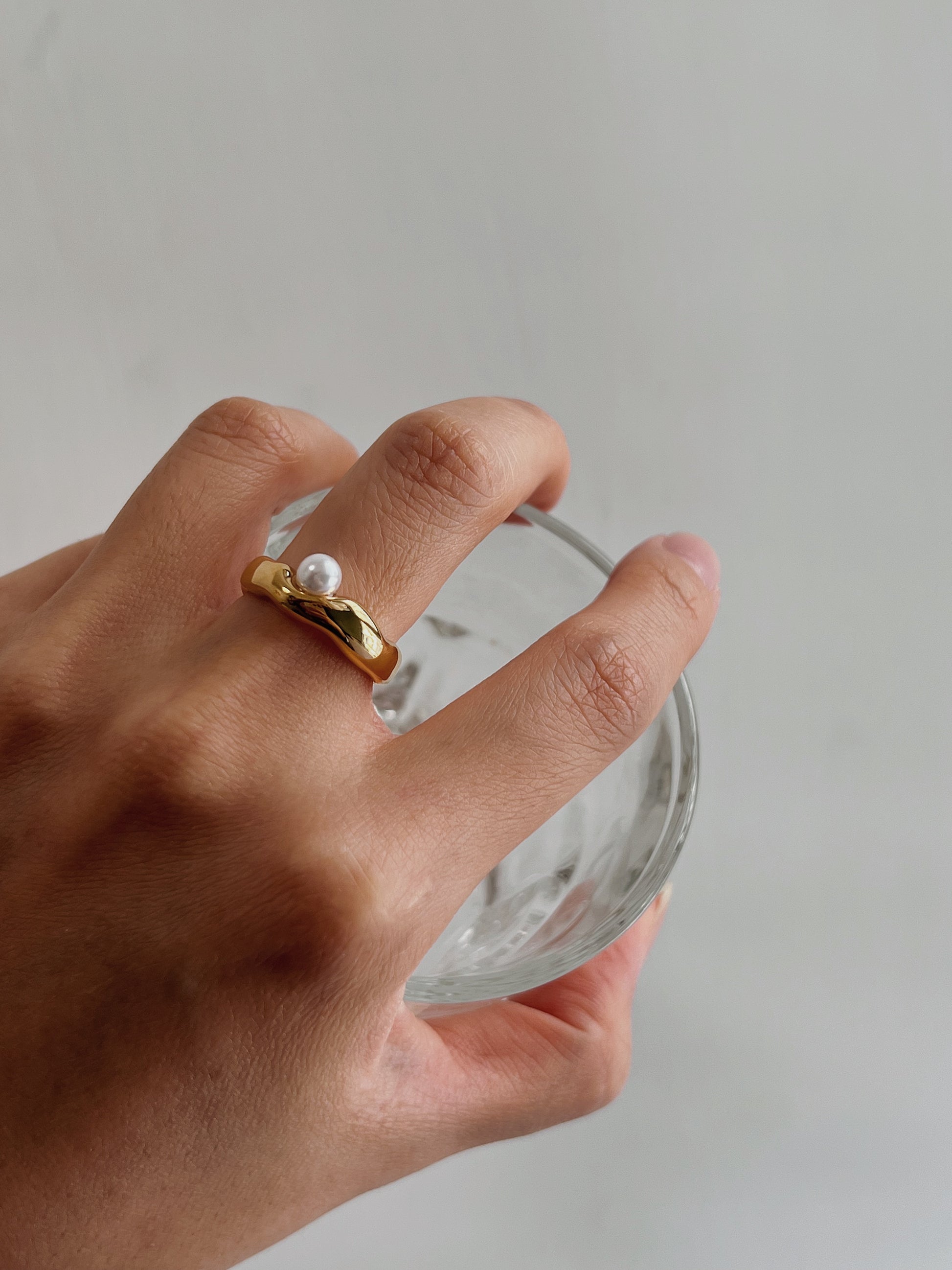 Close up of a single iridescent freshwater pearl resting on a wavy gold band.