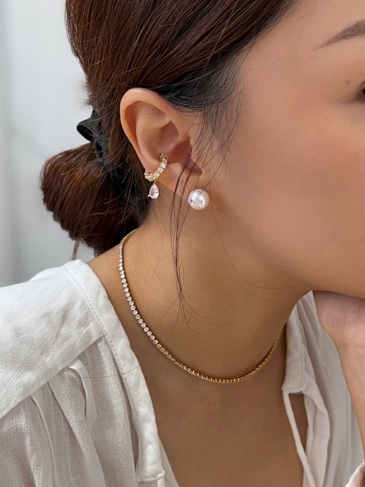 Editorial style jewelry lookbook photo highlighting high shine diamond style chains, diamond teardrop ear cuff and pearl studs on white top