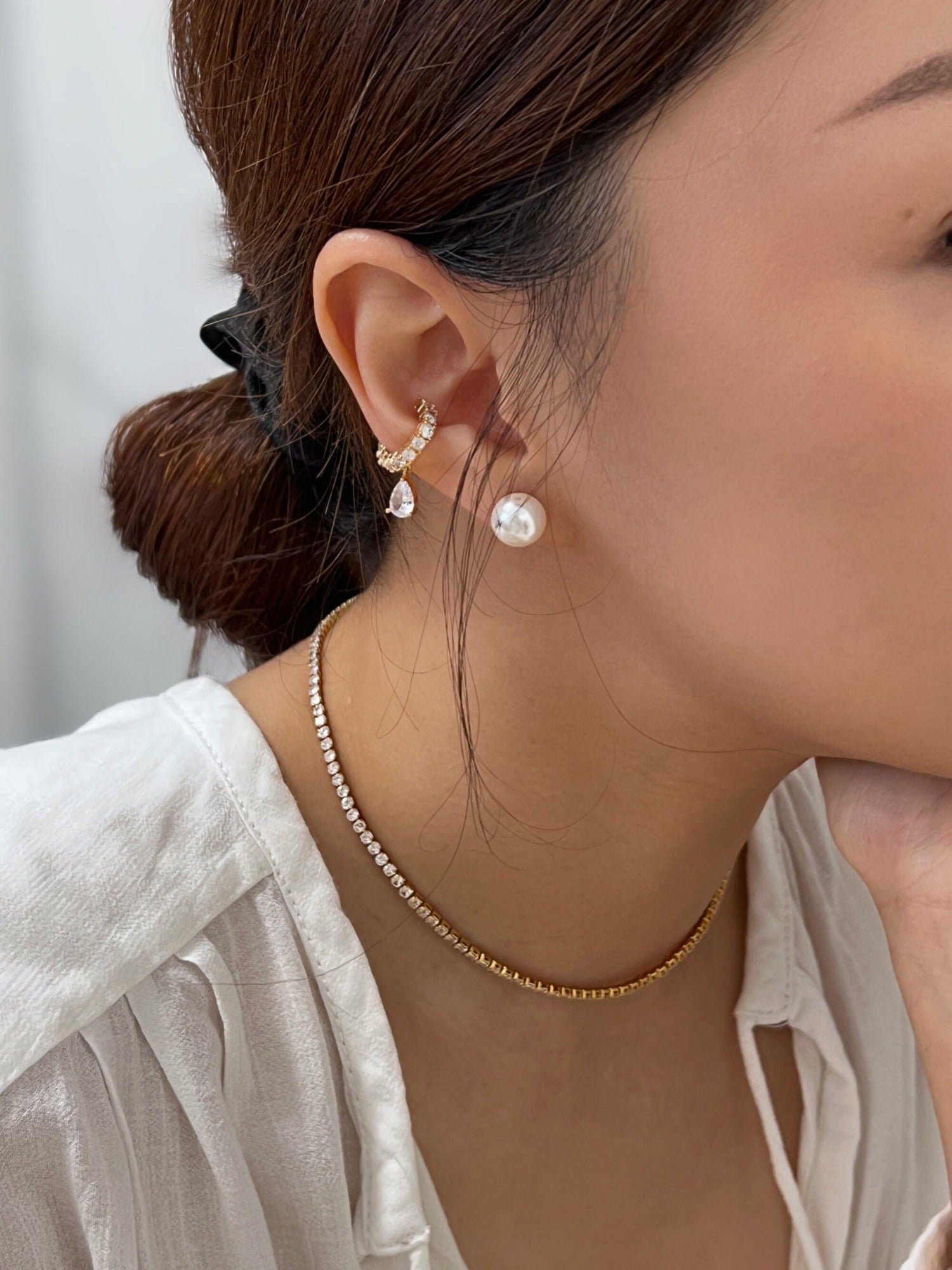 Editorial style jewelry lookbook photo highlighting high shine diamond style chains, diamond teardrop ear cuff and pearl studs on white top
