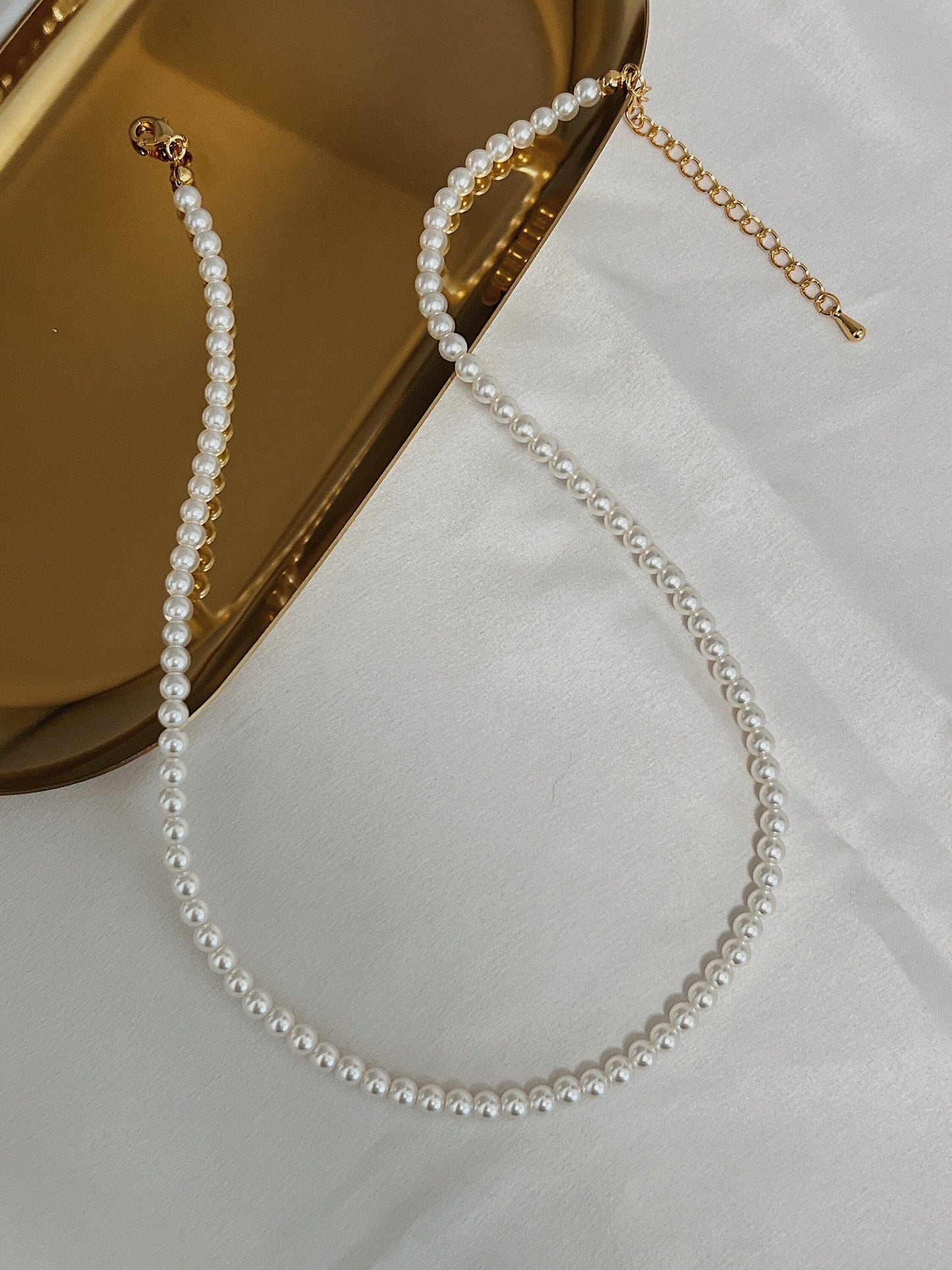 Close up view of fine high luster miniature pearl strand resting on reflective metal surface