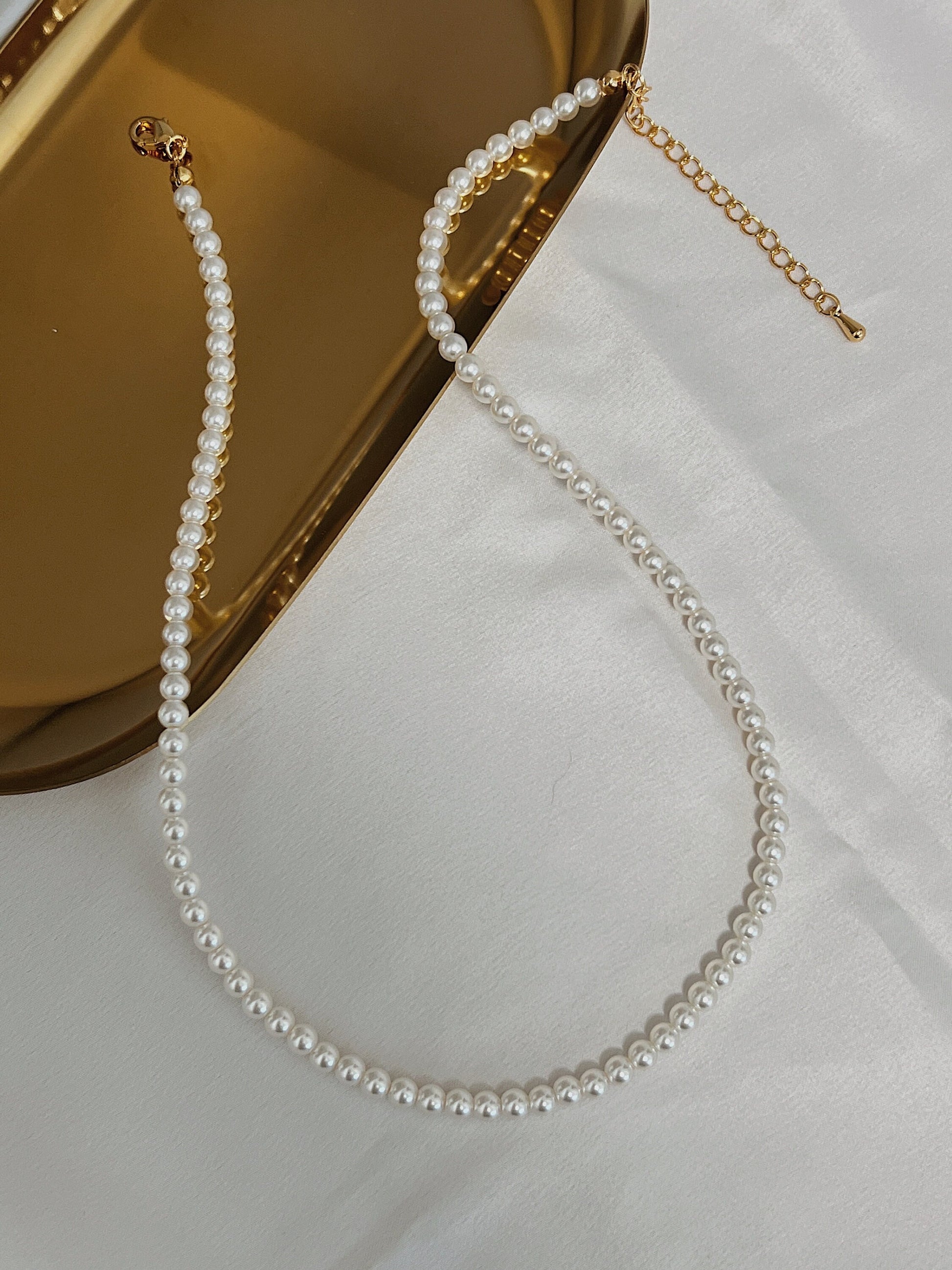 Close up view of fine high luster miniature pearl strand resting on reflective metal surface