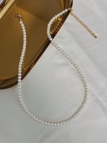 Close up view of fine high luster miniature pearl strand resting on reflective metal surface