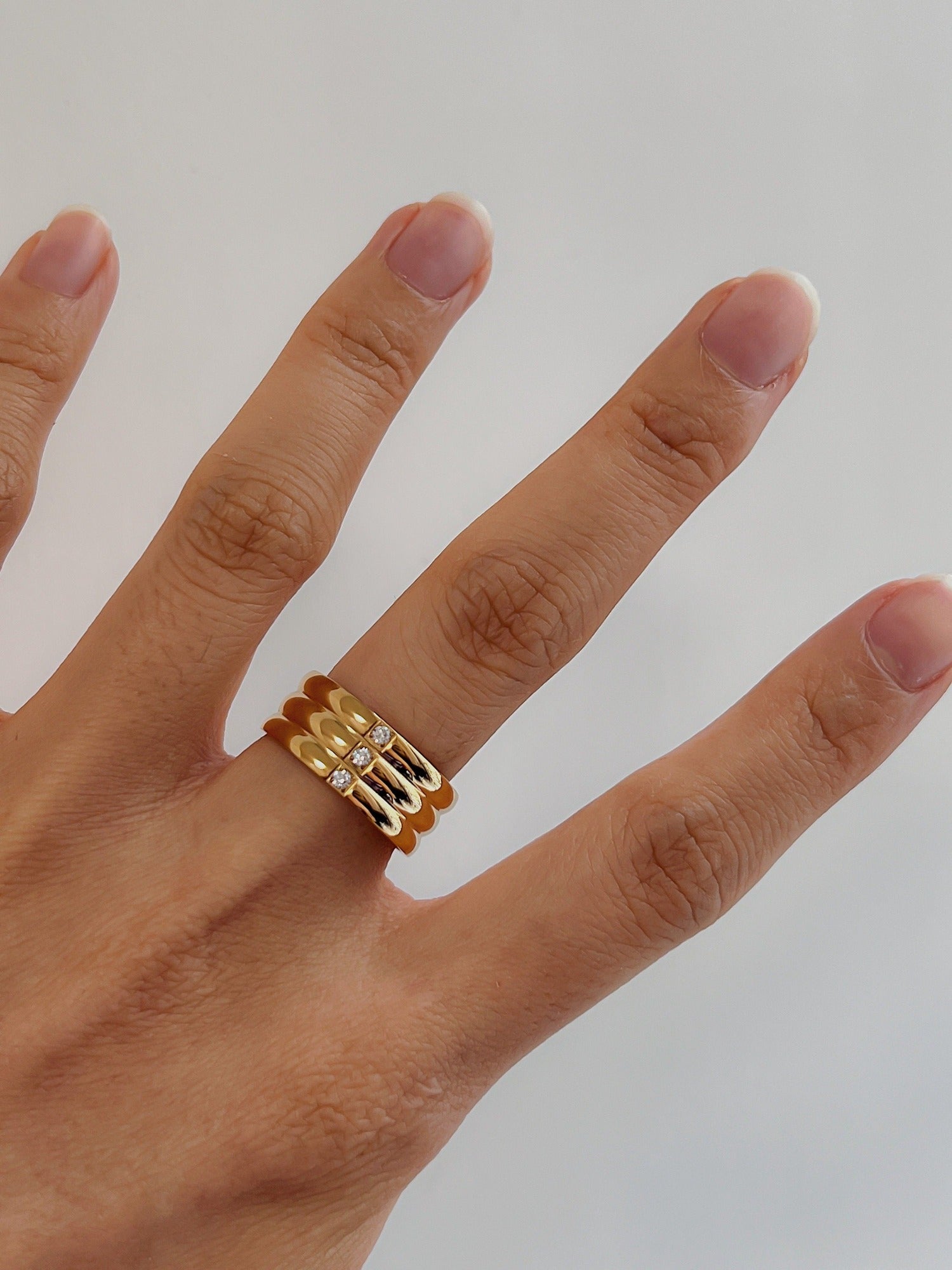 Close up of hand styling a gold wide statement band with neutral nails