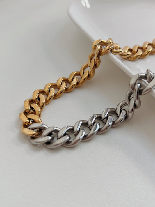 two tone cuban chain necklace displaying chunky gold and silver interlocking links on white surface