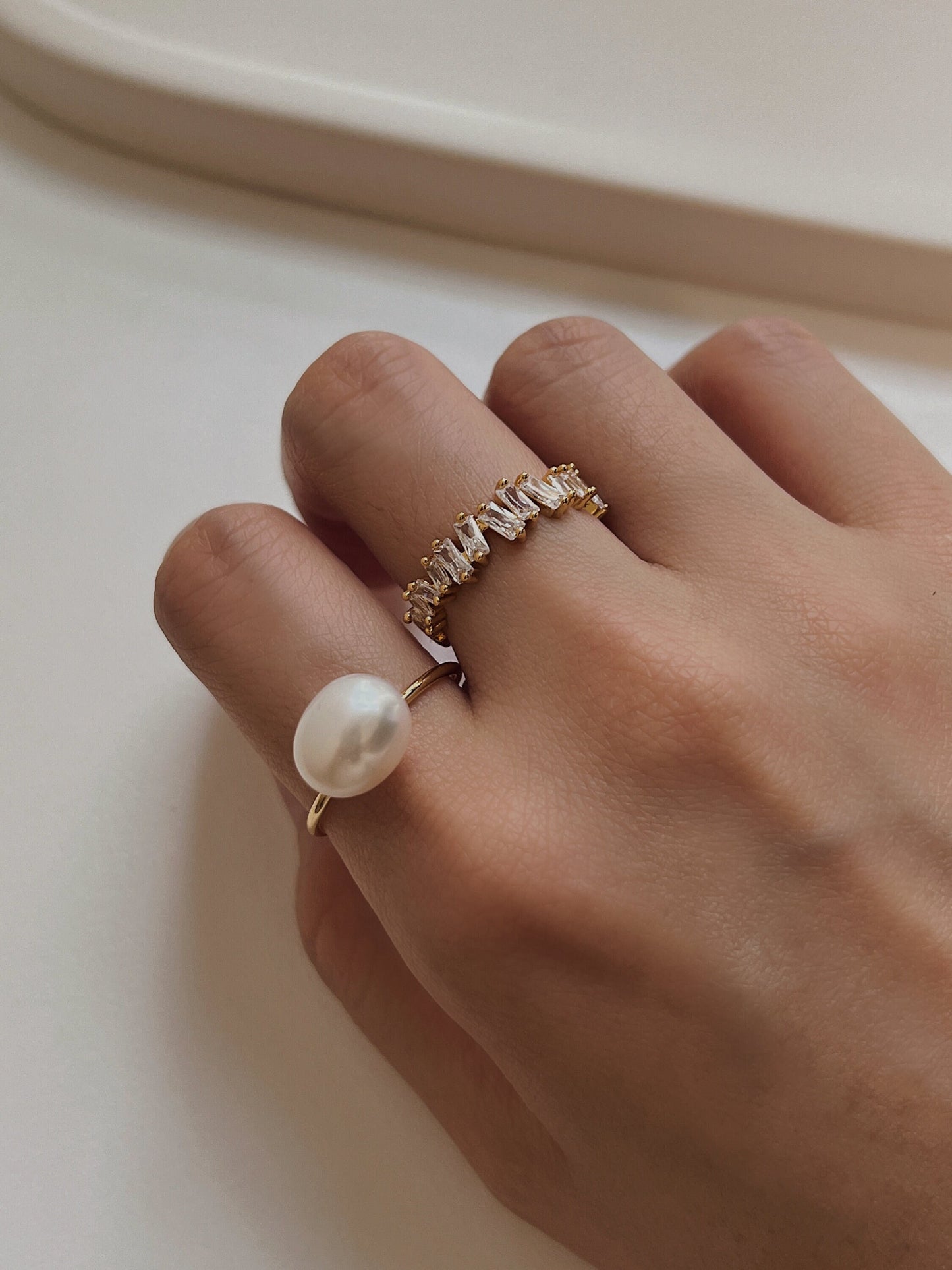 Close up of hand styling gold pearl rings and gold baguette ring for a high-end look