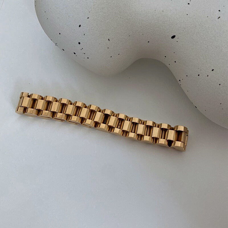 Top-down view of the wide 10mm gold watch link cuff bracelet on textured studio background.